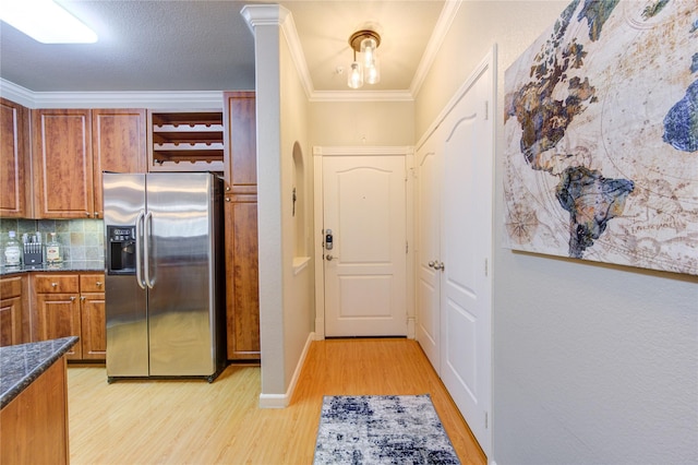 kitchen with tasteful backsplash, stainless steel fridge, crown molding, dark stone counters, and light hardwood / wood-style floors