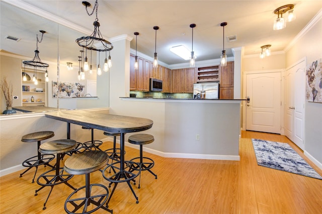 kitchen featuring kitchen peninsula, stainless steel appliances, crown molding, decorative light fixtures, and light hardwood / wood-style flooring