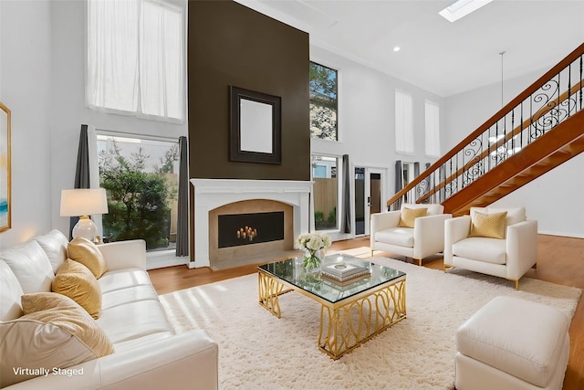 living room featuring hardwood / wood-style flooring, a healthy amount of sunlight, a towering ceiling, and a high end fireplace