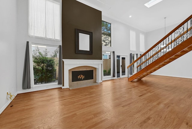 unfurnished living room with a high end fireplace, a healthy amount of sunlight, light hardwood / wood-style floors, and a high ceiling