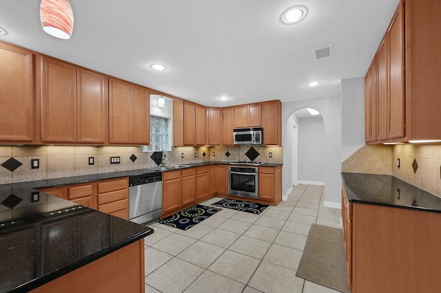 kitchen featuring sink, stainless steel appliances, dark stone countertops, and light tile patterned flooring