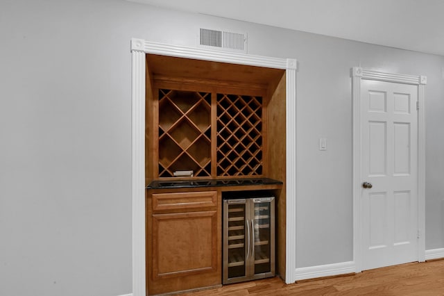 wine room with beverage cooler, indoor bar, and light wood-type flooring