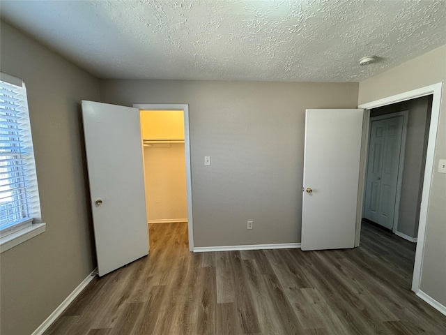 unfurnished bedroom with a textured ceiling, a closet, a spacious closet, and dark hardwood / wood-style flooring