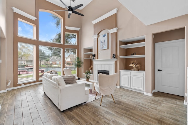 living room featuring built in shelves, ceiling fan, a tile fireplace, and a high ceiling