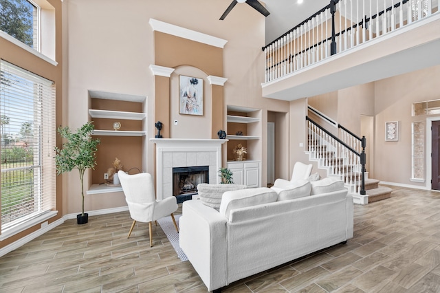 living room with ceiling fan, built in features, a fireplace, and a high ceiling