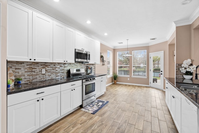 kitchen featuring dark stone counters, decorative backsplash, appliances with stainless steel finishes, decorative light fixtures, and white cabinetry