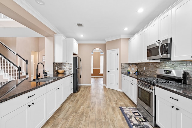 kitchen with white cabinetry, sink, stainless steel appliances, dark stone counters, and light hardwood / wood-style floors