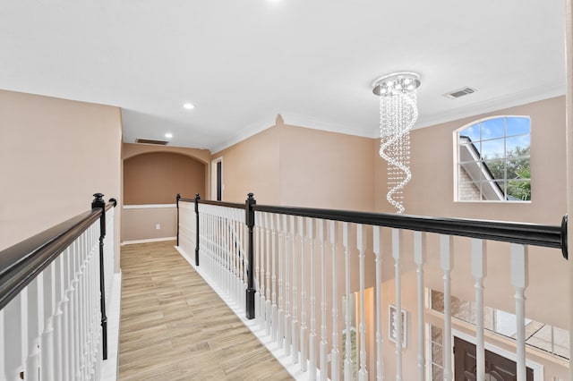 hallway featuring light hardwood / wood-style floors, ornamental molding, and an inviting chandelier