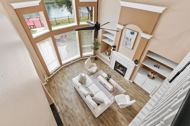 living room featuring wood-type flooring, a water view, a tiled fireplace, and a high ceiling