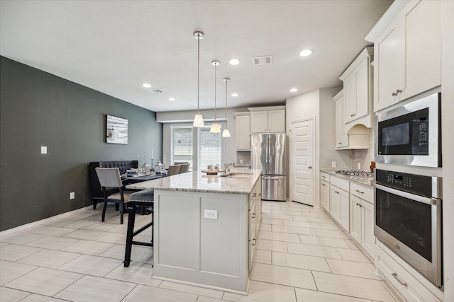 kitchen featuring a kitchen island with sink, sink, decorative light fixtures, white cabinetry, and stainless steel appliances