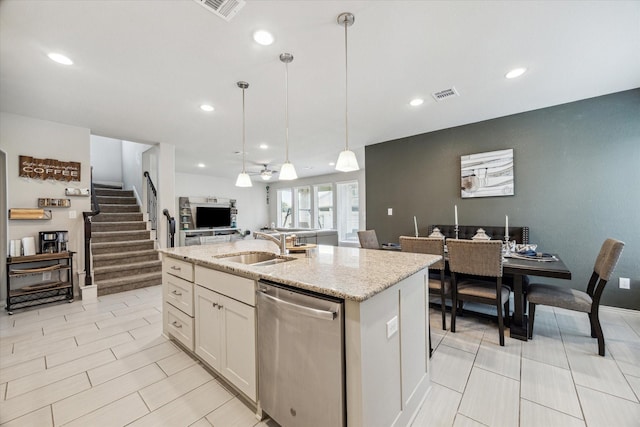 kitchen featuring light stone countertops, stainless steel dishwasher, white cabinets, hanging light fixtures, and an island with sink