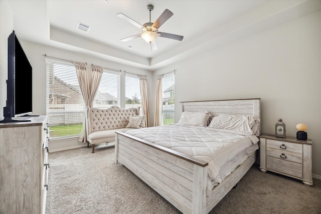 bedroom featuring ceiling fan, dark carpet, and a tray ceiling