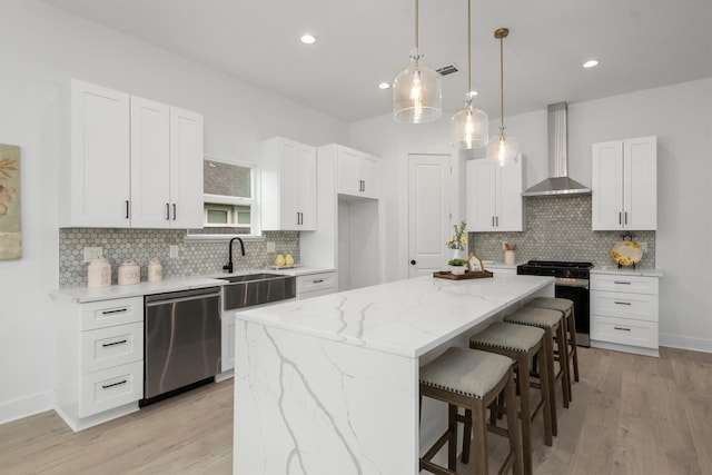 kitchen featuring white cabinetry, sink, wall chimney range hood, a kitchen island, and appliances with stainless steel finishes