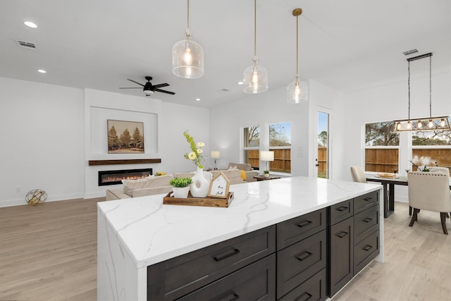 kitchen with light stone counters, decorative light fixtures, ceiling fan with notable chandelier, and light wood-type flooring