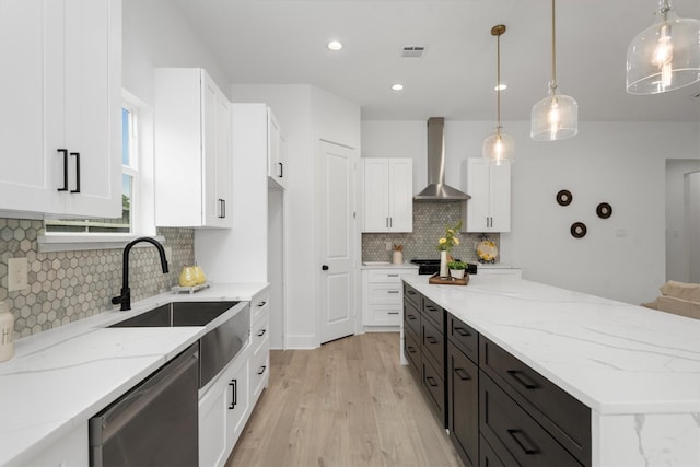 kitchen featuring white cabinets, sink, wall chimney range hood, decorative light fixtures, and dishwasher