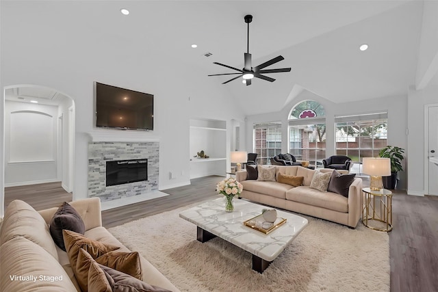 living room with a tile fireplace, ceiling fan, built in shelves, and wood-type flooring