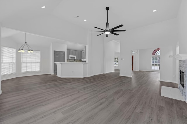 unfurnished living room featuring hardwood / wood-style flooring, ceiling fan with notable chandelier, a fireplace, and high vaulted ceiling