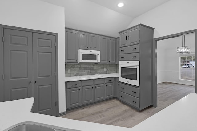 kitchen with lofted ceiling, white appliances, hanging light fixtures, tasteful backsplash, and a notable chandelier