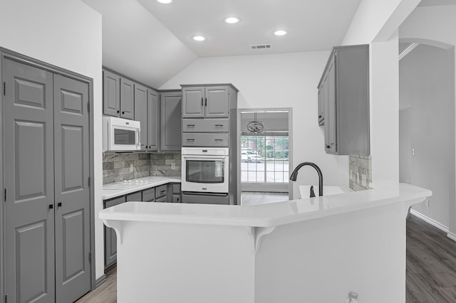 kitchen featuring kitchen peninsula, a kitchen breakfast bar, white appliances, and gray cabinets