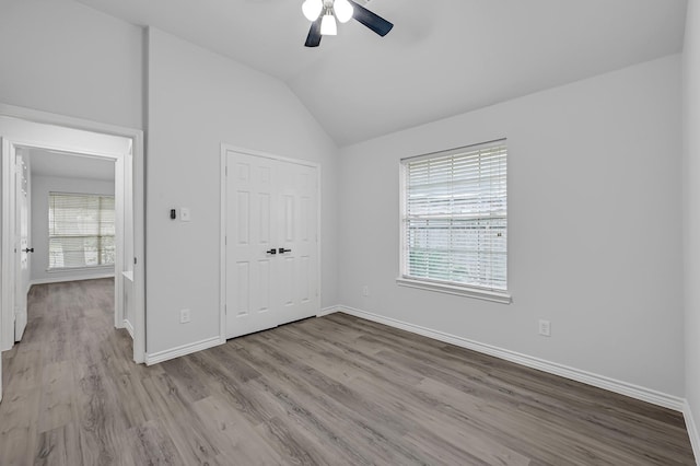 unfurnished bedroom with ceiling fan, a closet, lofted ceiling, and light hardwood / wood-style flooring