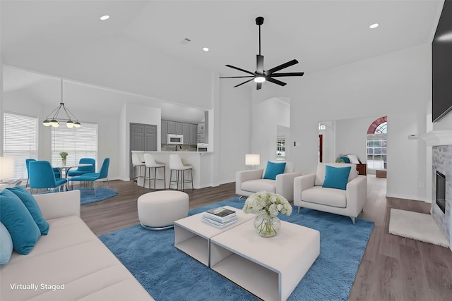 living room featuring a towering ceiling, hardwood / wood-style floors, ceiling fan with notable chandelier, and a healthy amount of sunlight