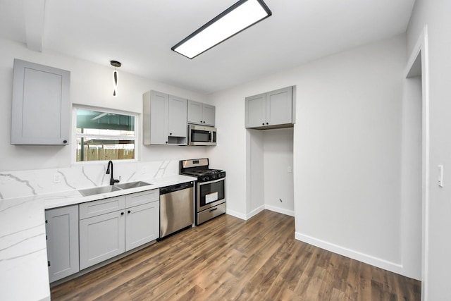 kitchen featuring sink, gray cabinetry, appliances with stainless steel finishes, dark hardwood / wood-style flooring, and light stone countertops