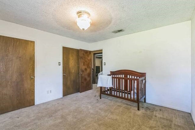 carpeted bedroom featuring ceiling fan, a textured ceiling, a nursery area, and a closet