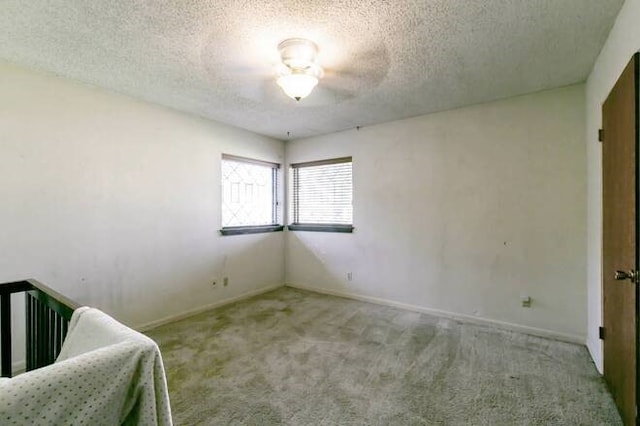 unfurnished bedroom with a textured ceiling, a nursery area, light colored carpet, and ceiling fan