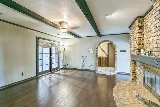 unfurnished living room featuring dark wood-type flooring, ceiling fan, a fireplace, a textured ceiling, and beamed ceiling