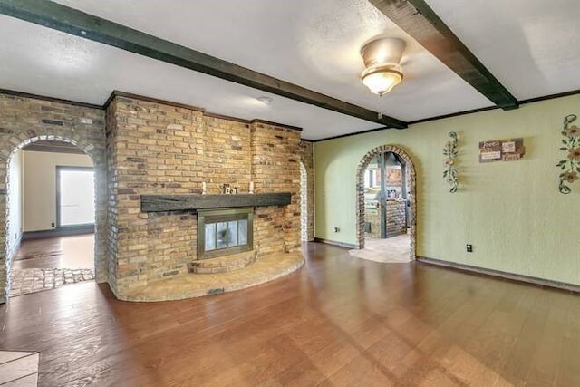 unfurnished living room featuring beam ceiling, hardwood / wood-style flooring, and a brick fireplace