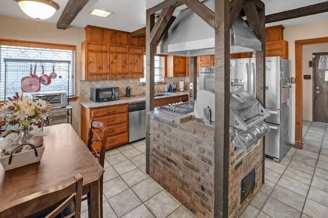 kitchen featuring backsplash, wall chimney range hood, light tile patterned floors, beamed ceiling, and stainless steel appliances