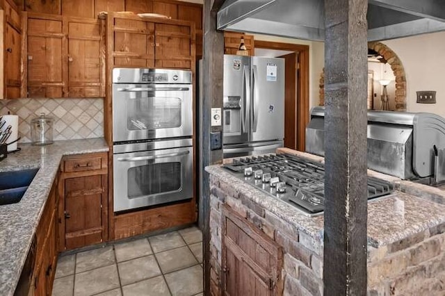 kitchen with tasteful backsplash, light stone counters, light tile patterned floors, and stainless steel appliances