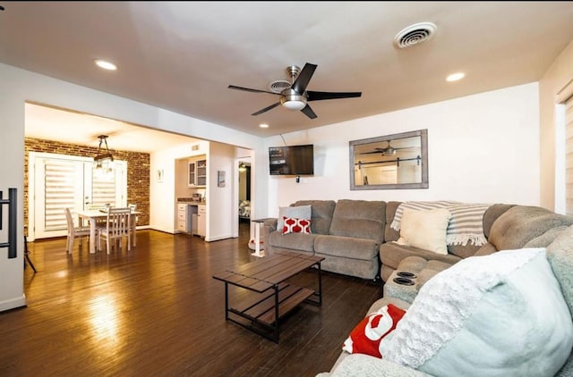 living room with ceiling fan, dark hardwood / wood-style flooring, and brick wall