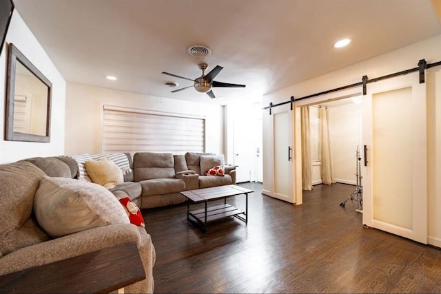 living room with a barn door, ceiling fan, and dark hardwood / wood-style flooring