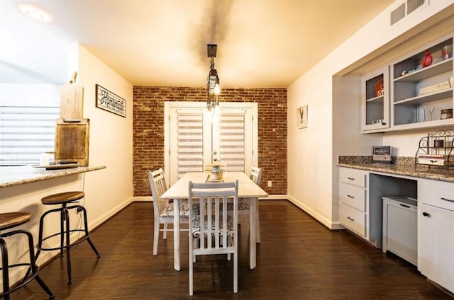 dining space featuring dark hardwood / wood-style flooring and brick wall