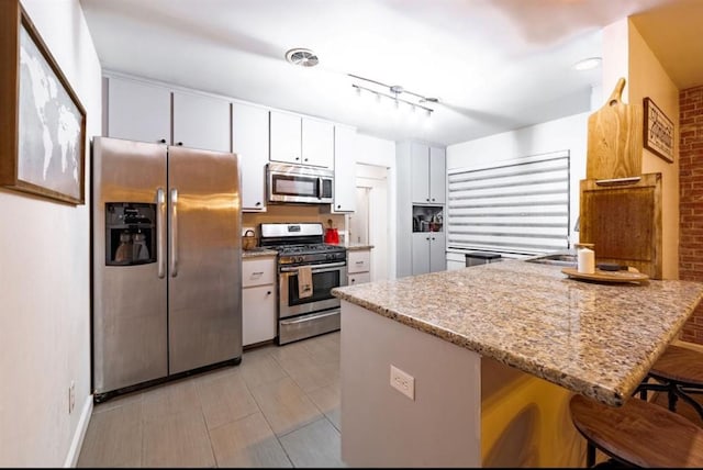 kitchen with kitchen peninsula, light stone counters, a breakfast bar, stainless steel appliances, and white cabinetry