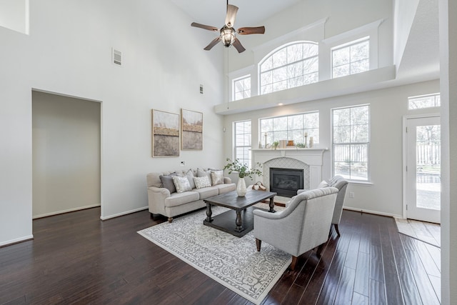 living room featuring a towering ceiling, dark wood-type flooring, a tile fireplace, and ceiling fan