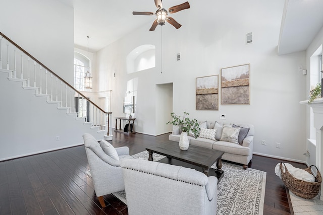 living room with a high ceiling, dark wood-type flooring, and ceiling fan with notable chandelier