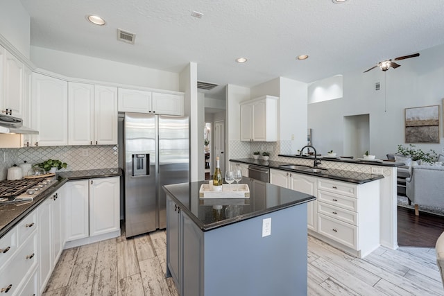 kitchen with sink, appliances with stainless steel finishes, extractor fan, white cabinets, and a kitchen island