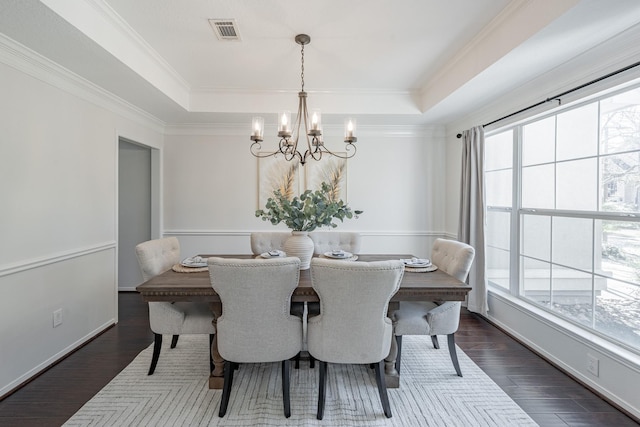 dining space with crown molding, dark wood-type flooring, an inviting chandelier, and a tray ceiling