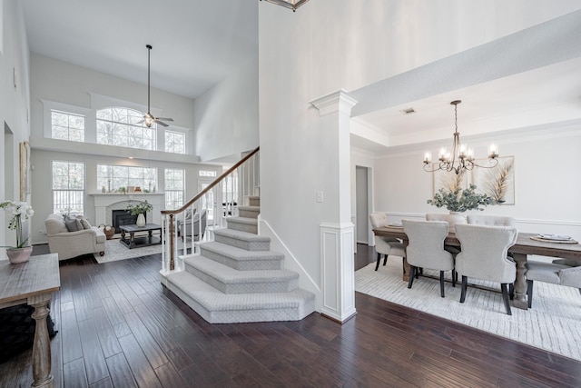 entrance foyer with ornate columns, a tray ceiling, dark hardwood / wood-style floors, a towering ceiling, and ceiling fan with notable chandelier