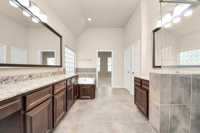 bathroom with tile patterned floors, vanity, a tub, and vaulted ceiling