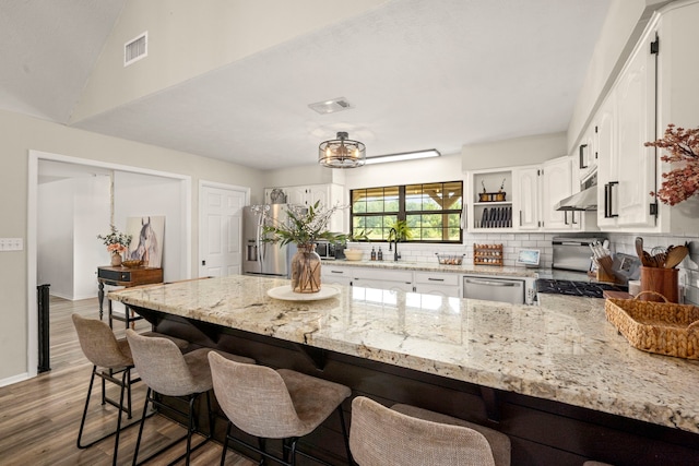 kitchen featuring a kitchen bar, backsplash, light stone counters, stainless steel appliances, and white cabinets