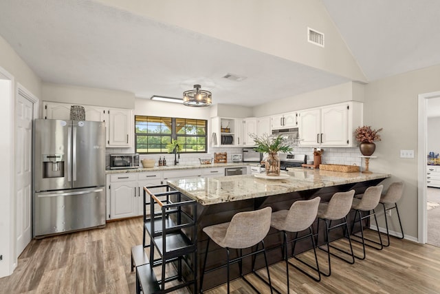 kitchen featuring sink, light stone counters, appliances with stainless steel finishes, a kitchen bar, and white cabinetry