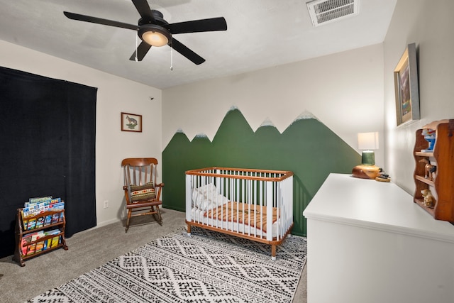 carpeted bedroom with ceiling fan and a crib