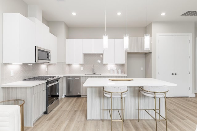 kitchen featuring pendant lighting, white cabinets, tasteful backsplash, a kitchen island, and stainless steel appliances