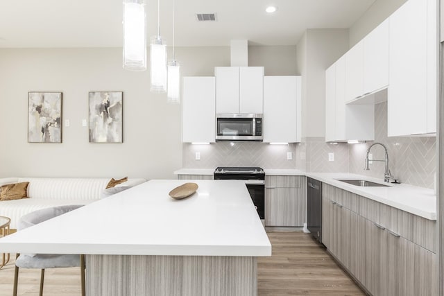 kitchen featuring hanging light fixtures, white cabinets, stainless steel appliances, and sink