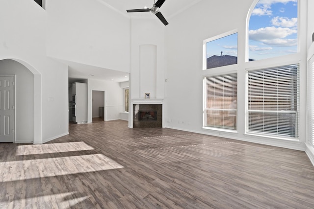 unfurnished living room with wood-type flooring, a towering ceiling, ceiling fan, and crown molding