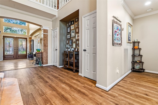 entrance foyer with french doors, a high ceiling, decorative columns, crown molding, and hardwood / wood-style flooring