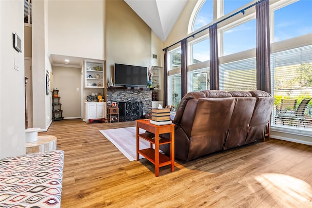 living room featuring light wood-type flooring, high vaulted ceiling, and a stone fireplace